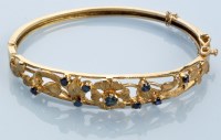 Lot 977 - A 9ct. yellow gold and sapphire bangle, the...