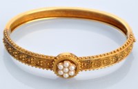 Lot 688 - A yellow metal and half pearl bangle, of...