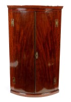 Lot 1210 - A George III mahogany bowfront corner cabinet,...