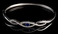 Lot 957 - A sapphire and diamond bangle, the central...