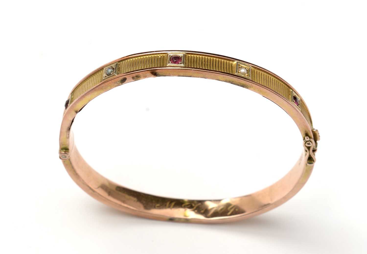 Lot 89 - An Edwardian 9ct gold, garnet, and pearl bangle of Etruscan influence.