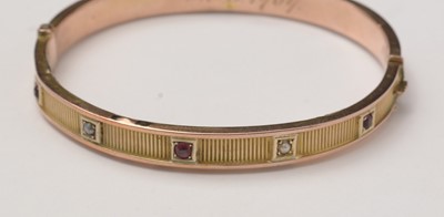 Lot 89 - An Edwardian 9ct gold, garnet, and pearl bangle of Etruscan influence.