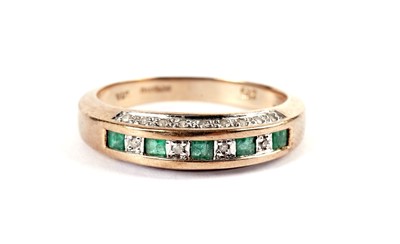 Lot 502 - A diamond and emerald half hoop eternity ring