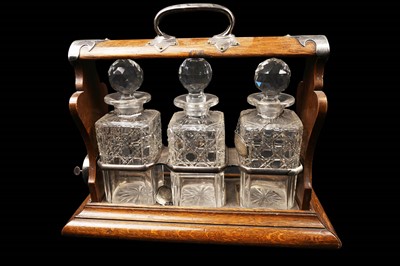 Lot 272 - ﻿An early 20th Century oak three bottle tantalus with silver plated mounts by Walker & Hall