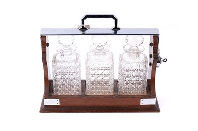 Lot 138 - An early 20th Century three bottle Tantalus; and three ‘Hobnail’ cut decanters