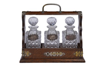 Lot 235 - An early 20th Century oak three bottle tantalus, each with silver wine label